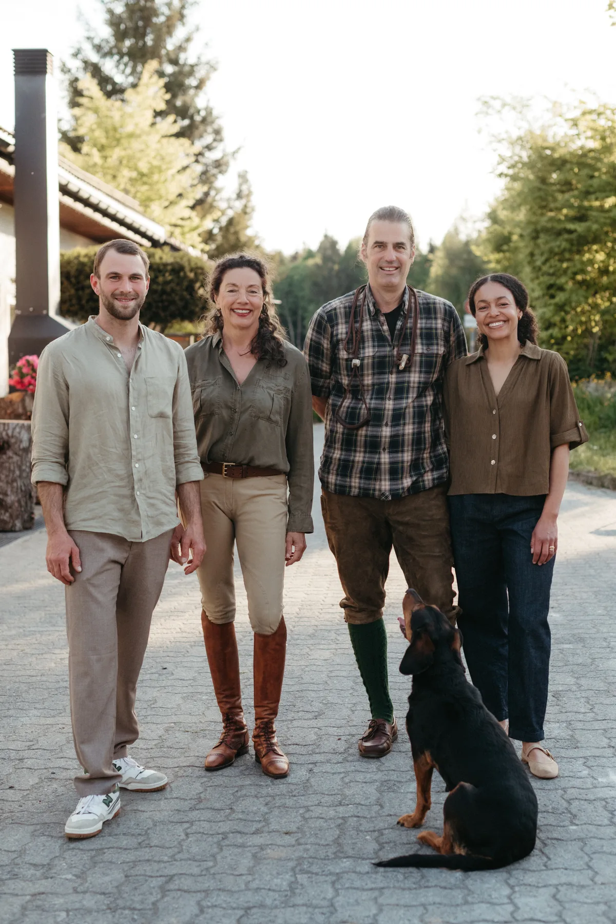 Zu viert hauchen sie dem «Waldhof Guldenen» wieder Leben ein: das Landwirtepaar Claudia Wanger und Nils Müller (Mitte) und das Ehepaar Benjamin und Rose Plšek (aussen). Vier Personen stehen auf einem Vorplatz vor einem Gebäude. Vor den Personen sitzt ein Hund und blickt hoch zu den Menschen.